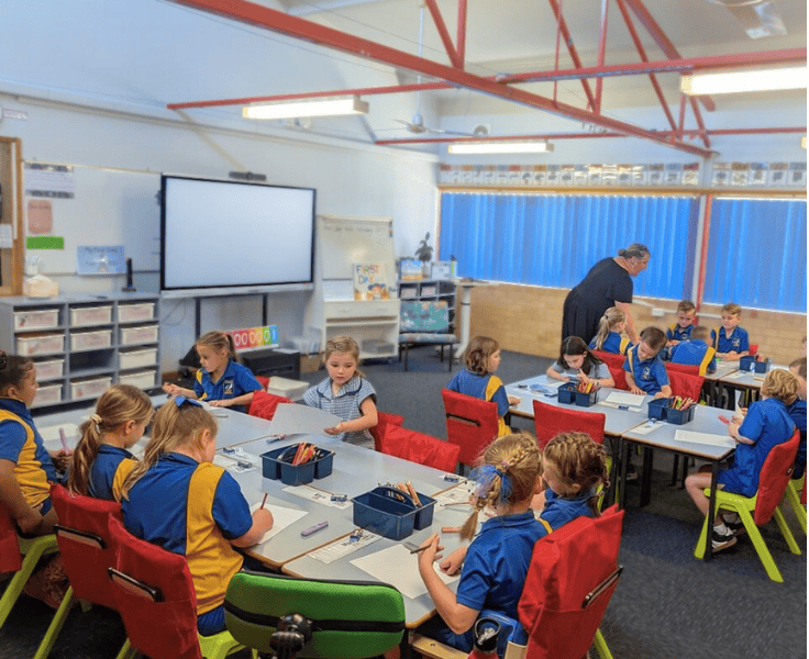 Students working at desks in a large bright classroom.