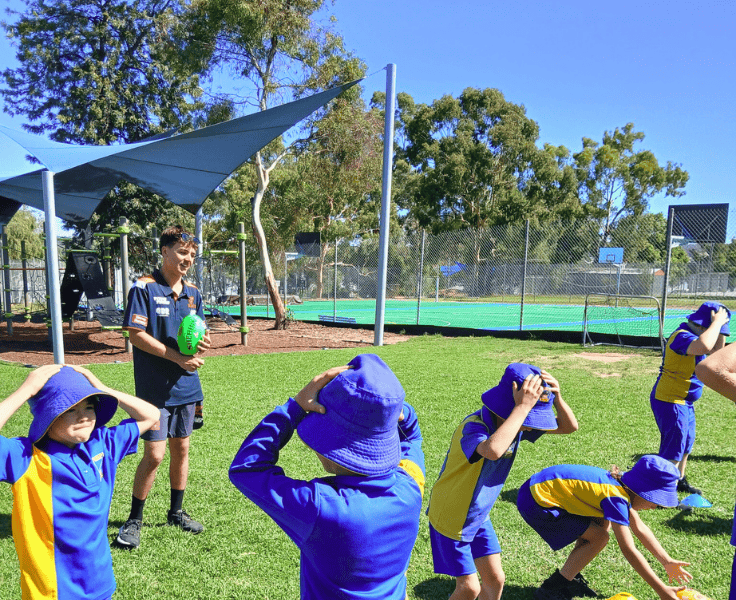 Several students playing a game in front of a playground and tennis courts.