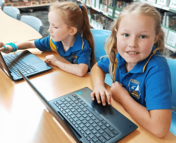 Two students on using laptoos at a desk in the library.