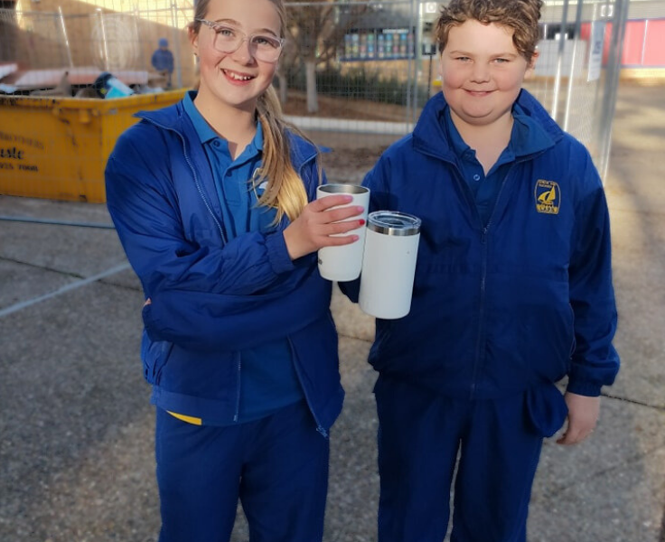 Two students holding reusable mugs and wearing the LAPS winter uniform.